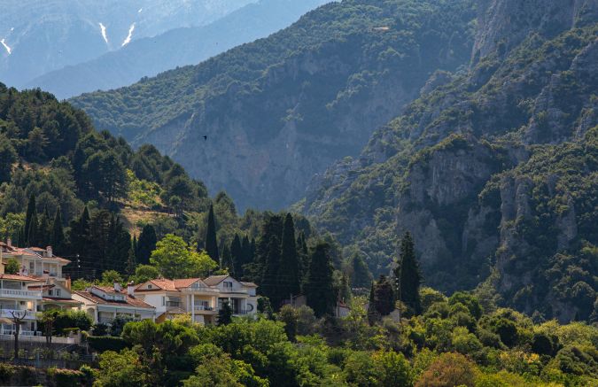 A scenic view of Litochoro town with traditional houses at the foot of the lush green cliffs of Mount Olympus, Greece